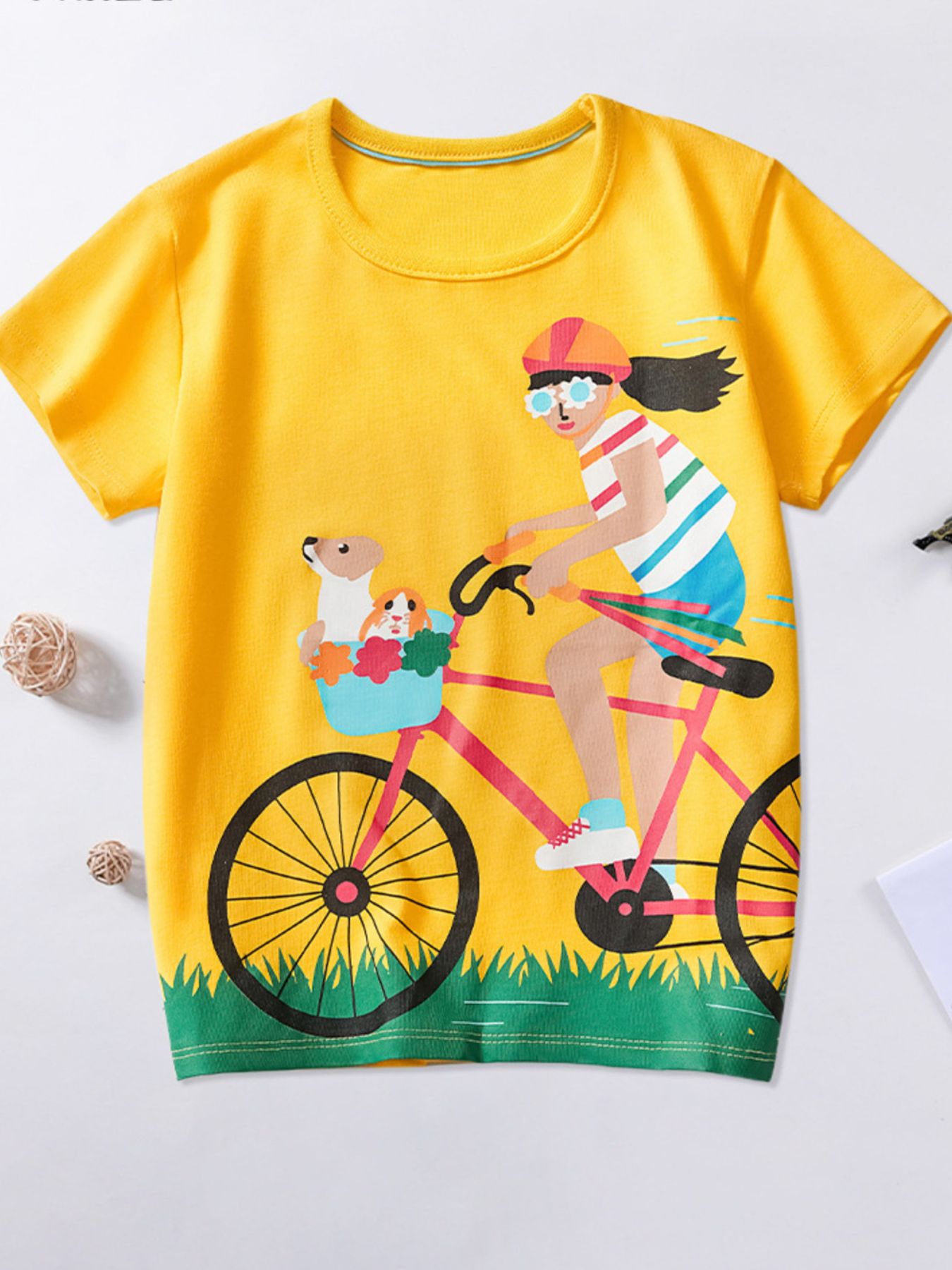 Flat front view of yellow children's t-shirt with cyclist on pink bicycle graphic