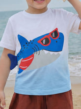 Close-up front view of children's white to light blue T-shirt with a blue shark wearing red sunglasses