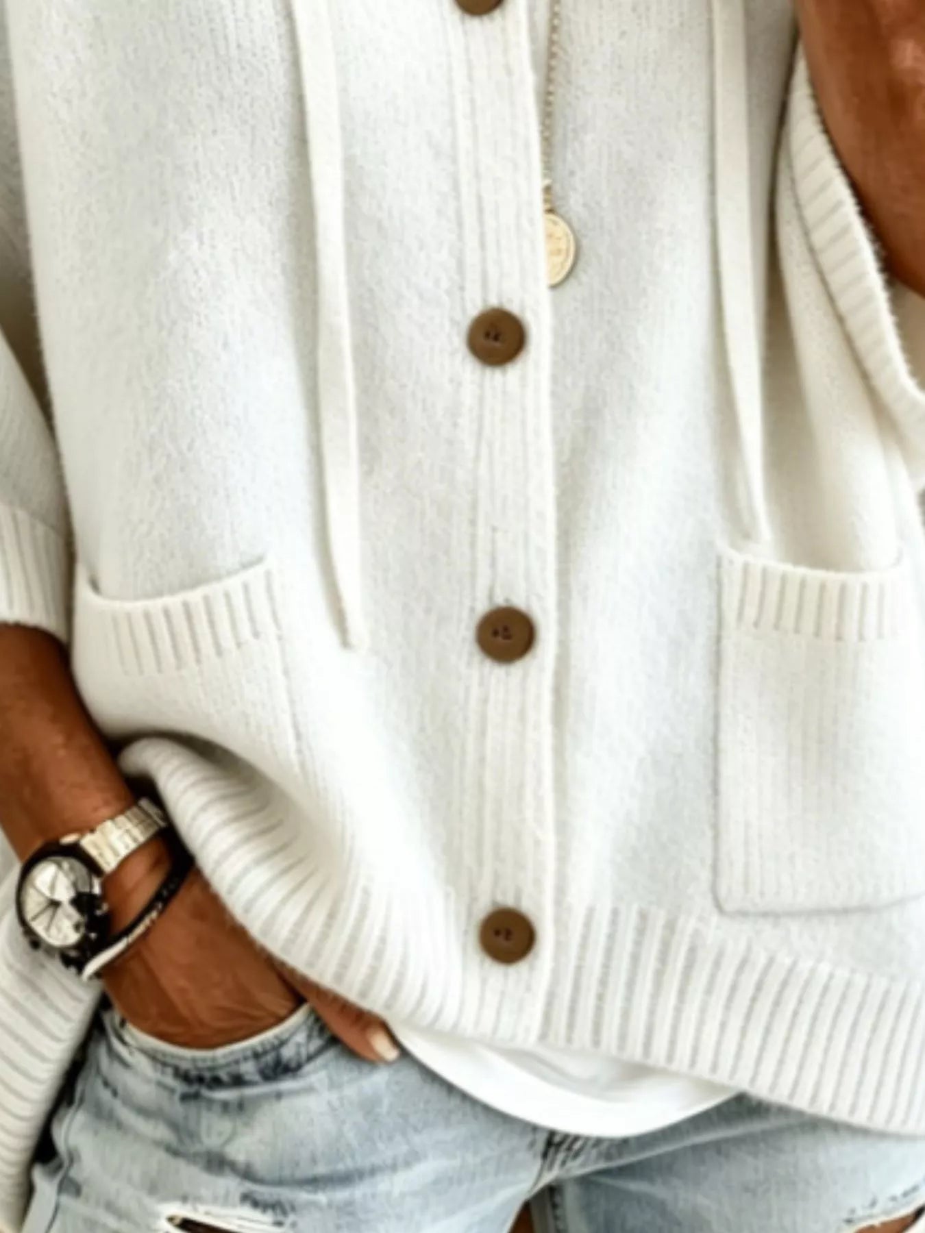 Detail view of the white cardigan showing brown buttons, patch pockets and ribbed hem
