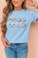 Model wearing a light blue relaxed T-shirt with floral-print “1776” and America script graphic.