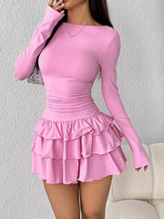 Pink long sleeve mini dress worn front facing with one hand raised near the face