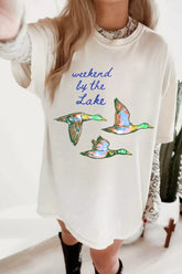 White oversized T-shirt featuring blue “weekend by the Lake” lettering and three colorful flying ducks.