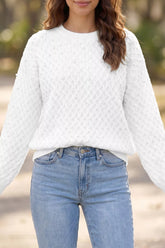 On-model front view of white textured knit pullover sweater with scattered pearl embellishments outdoors