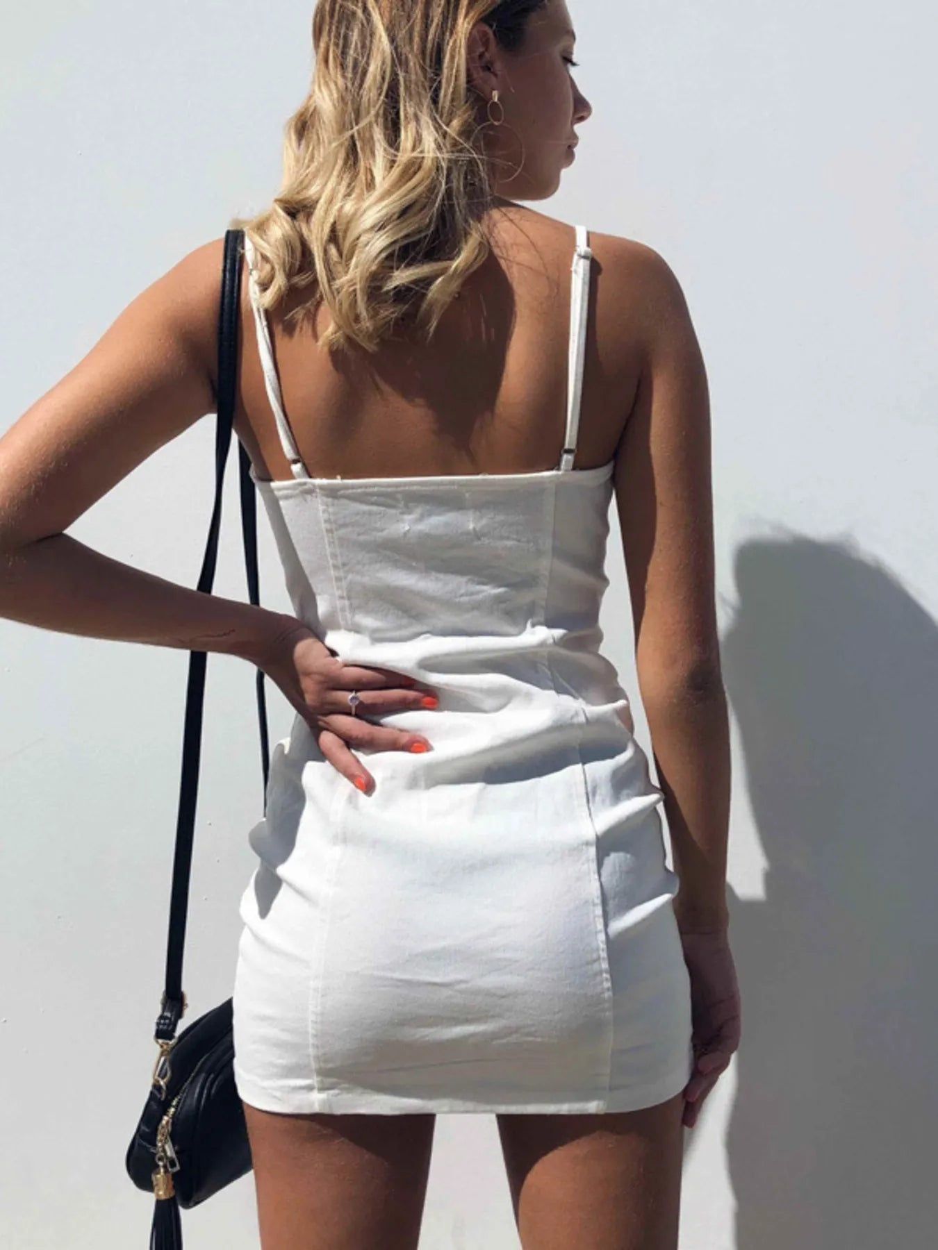 Back view of white zip front bodycon mini dress on model carrying a black shoulder bag