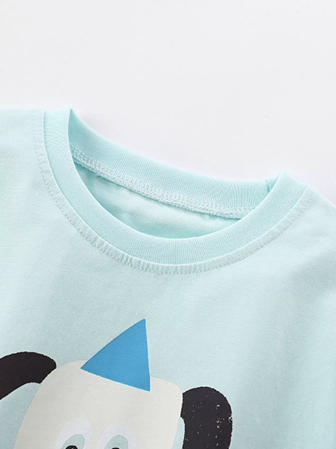 Close-up of mint blue children's t-shirt crew neckline and stitching, with cartoon dog below