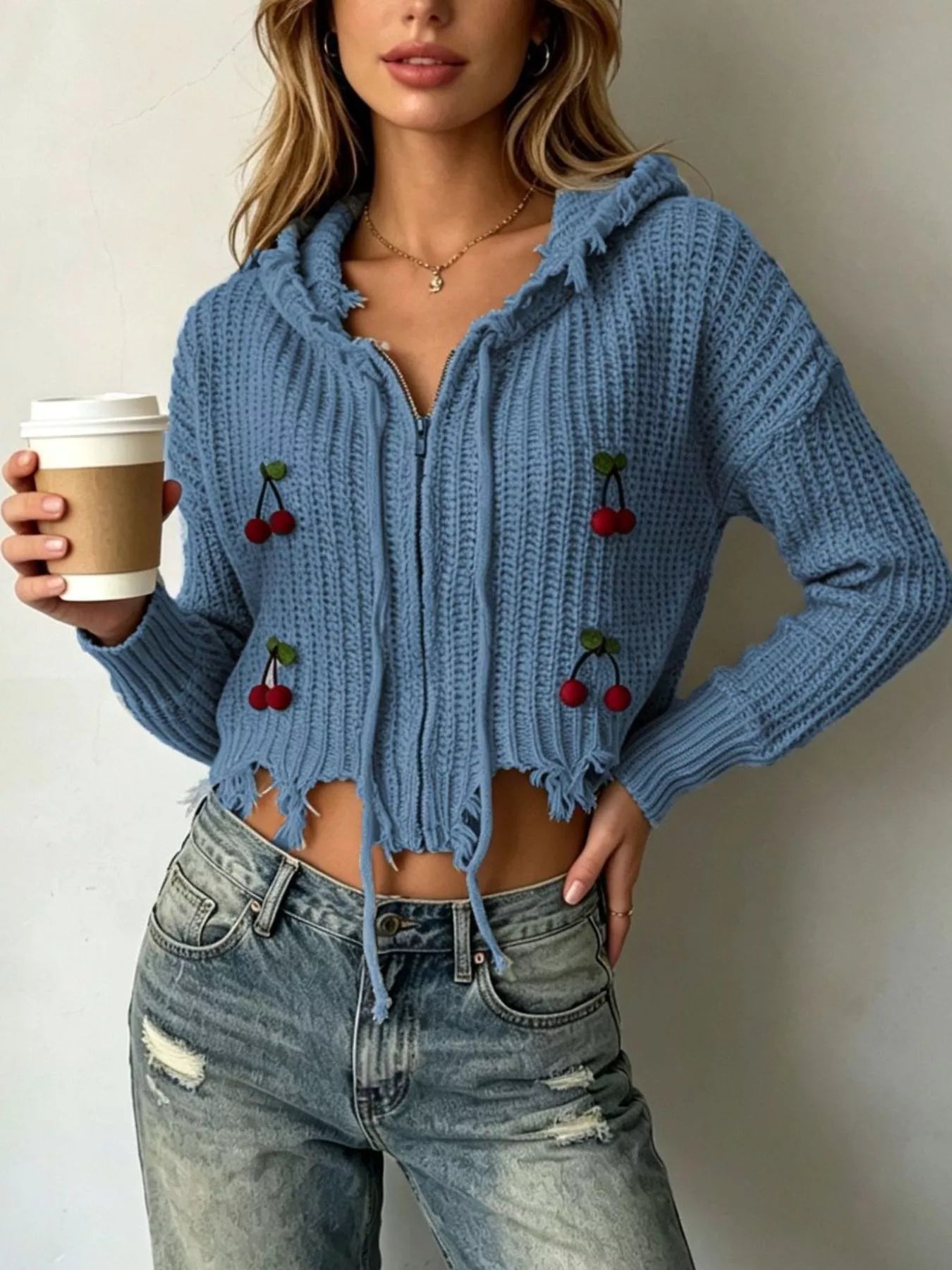 Dark blue knit zip up hooded sweater with red cherry appliques worn on model holding coffee