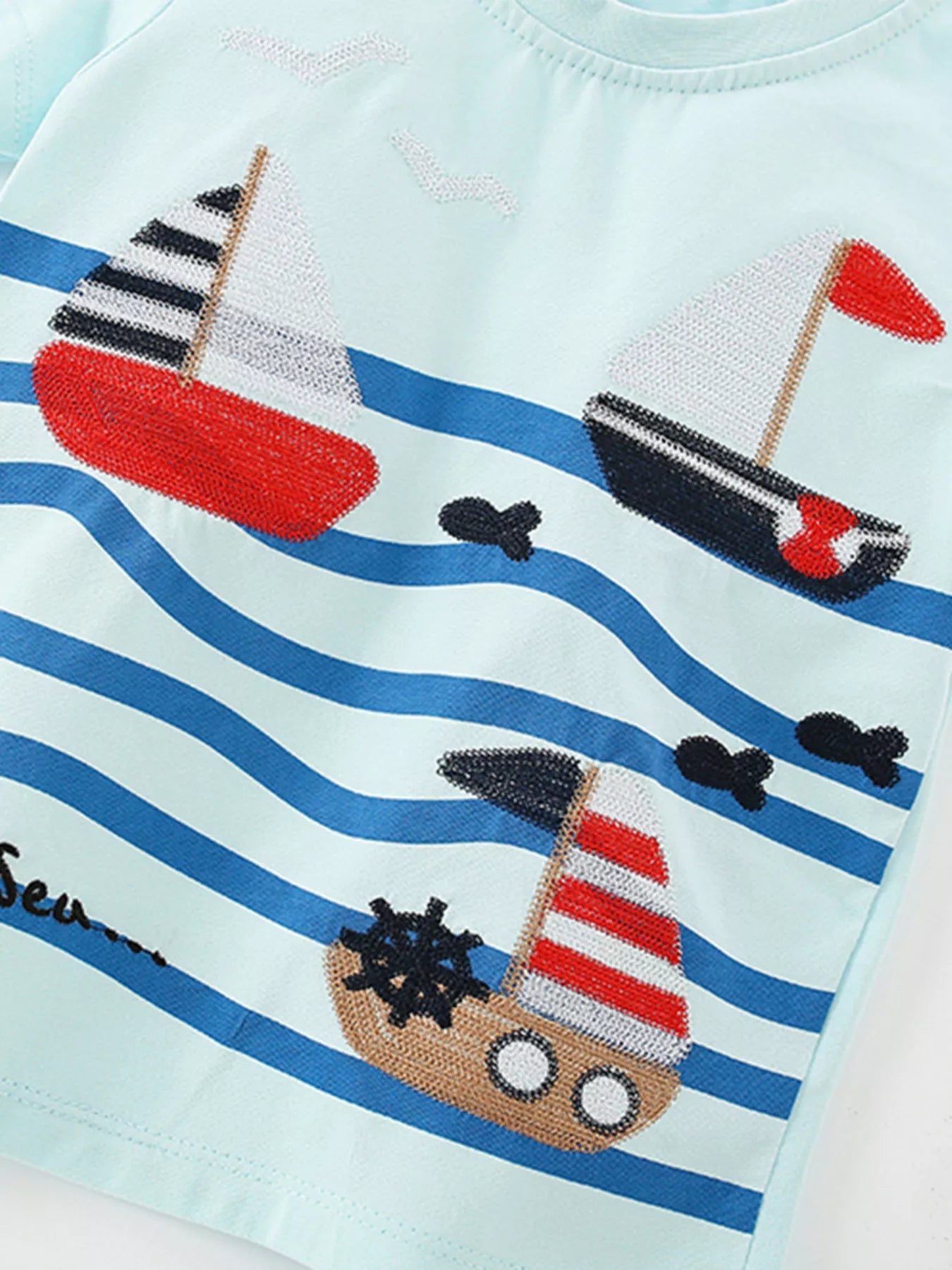 Angled close-up of the embroidered sailboats, waves, and small fish on mint blue fabric
