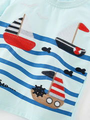 Angled close-up of the embroidered sailboats, waves, and small fish on mint blue fabric