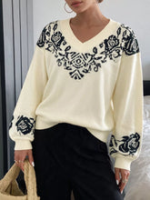Front view of a cream sweater with black floral knit pattern across the chest and sleeves