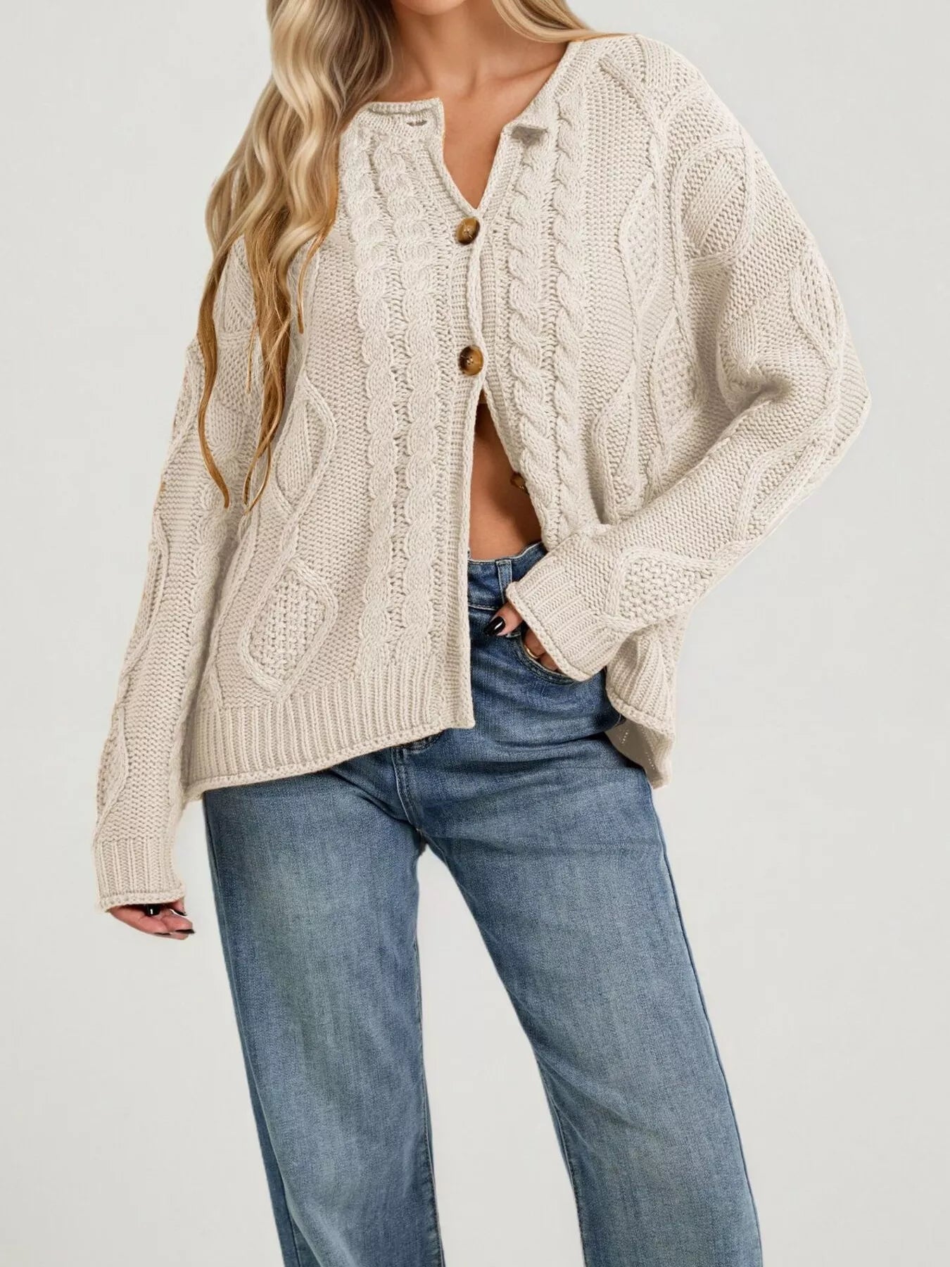 Front view of cream cable knit button down cardigan with brown buttons and blue jeans