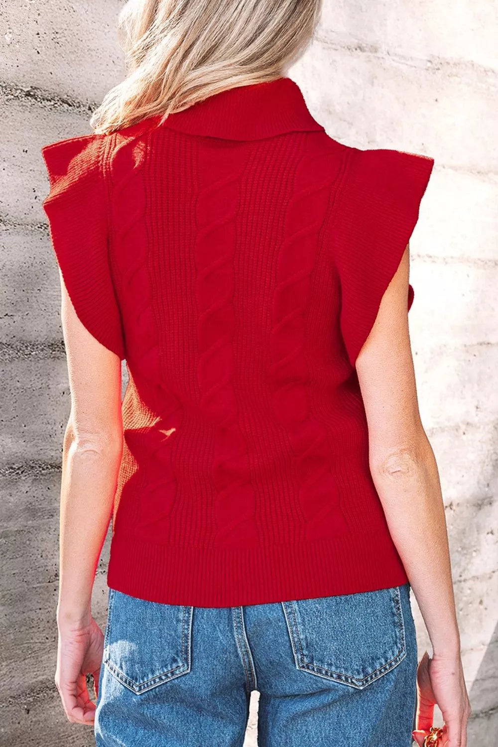 Outdoor back view of a red cable knit turtleneck sweater with ruffled short sleeves