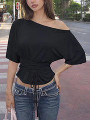 Black boat-neck short-sleeve top with ruched waist tie, modeled with jeans in a street setting
