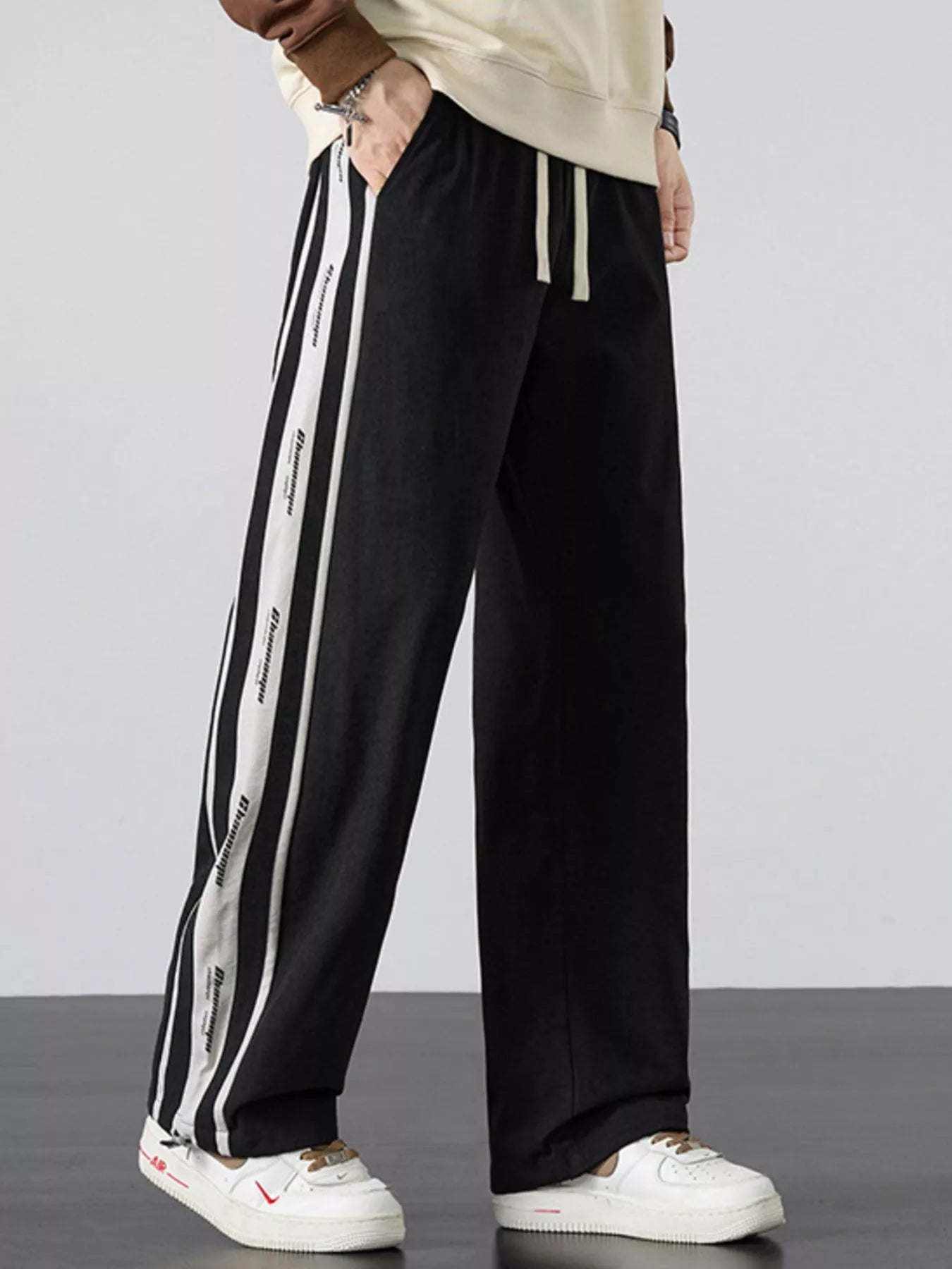 Men's black loose-fit pants with side stripes and a drawstring waist.