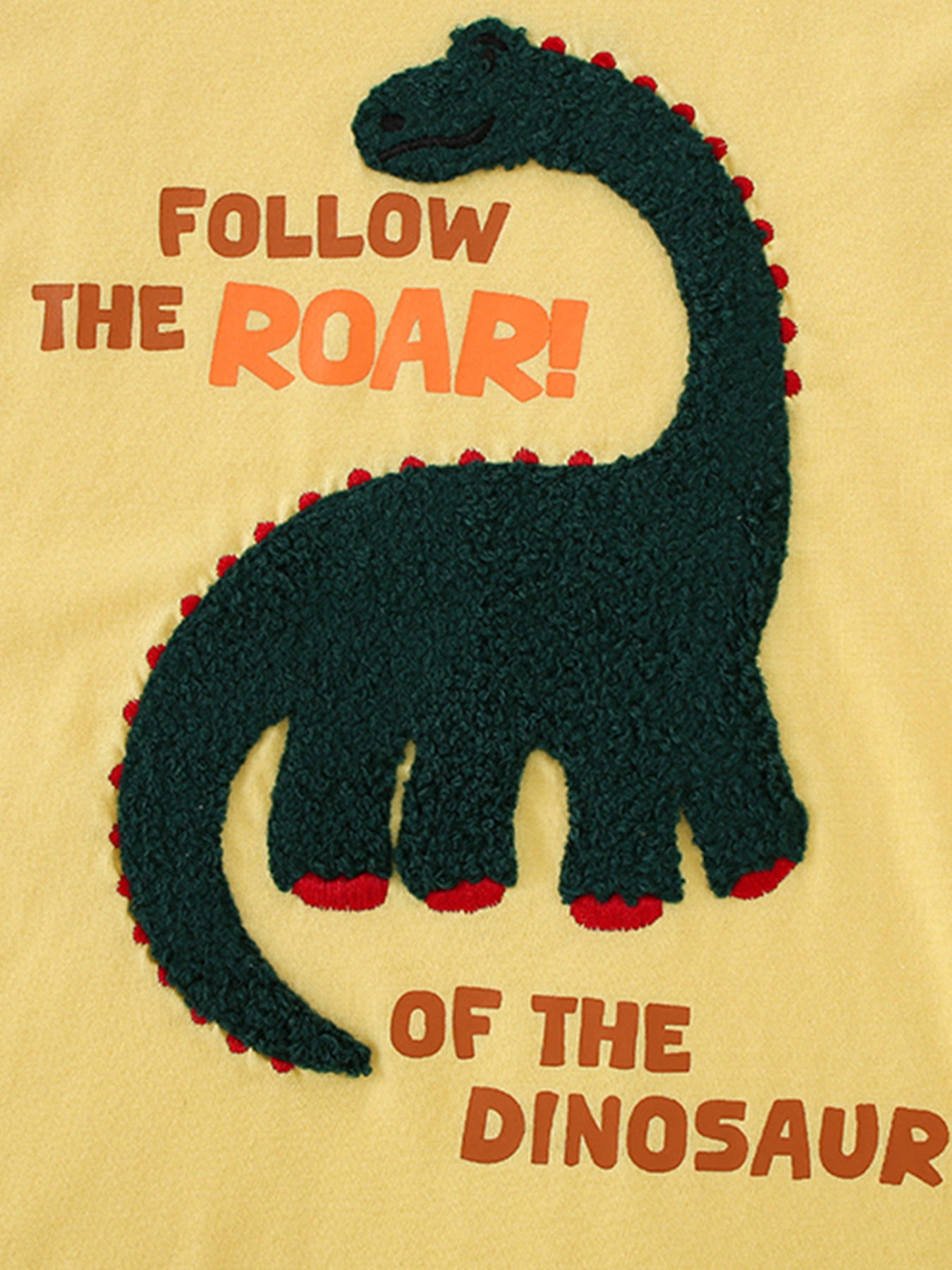 Close-up of the dark green textured dinosaur graphic on a yellow children's round neck T-shirt