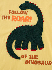 Close-up of the dark green textured dinosaur graphic on a yellow children's round neck T-shirt