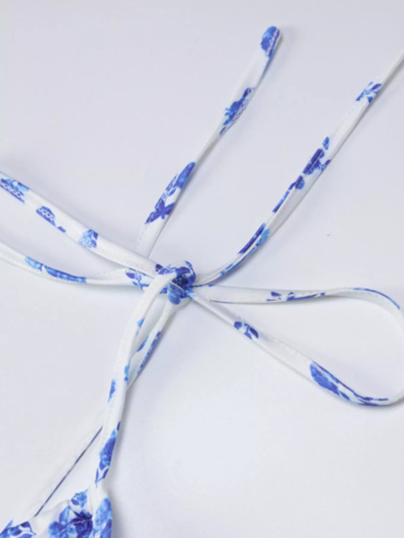 Close up of blue floral print tie straps tied in a knot on white background