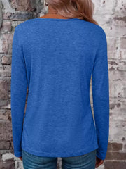 Back view of a blue long-sleeve V-neck top modeled with jeans against a brick wall