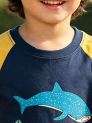 Close-up of the dark navy neckline and yellow raglan sleeve above a spotted shark