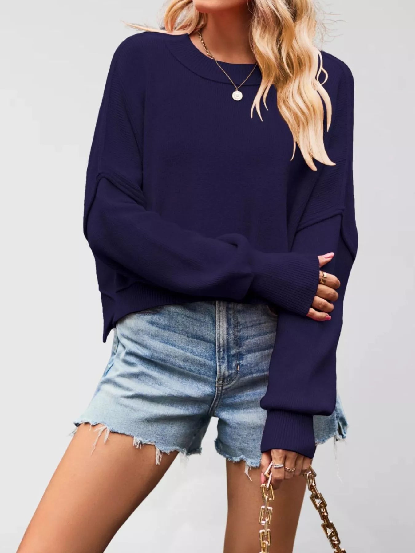 Front view of a dark navy crew neck dropped shoulder sweater with ribbed cuffs worn with denim shorts.