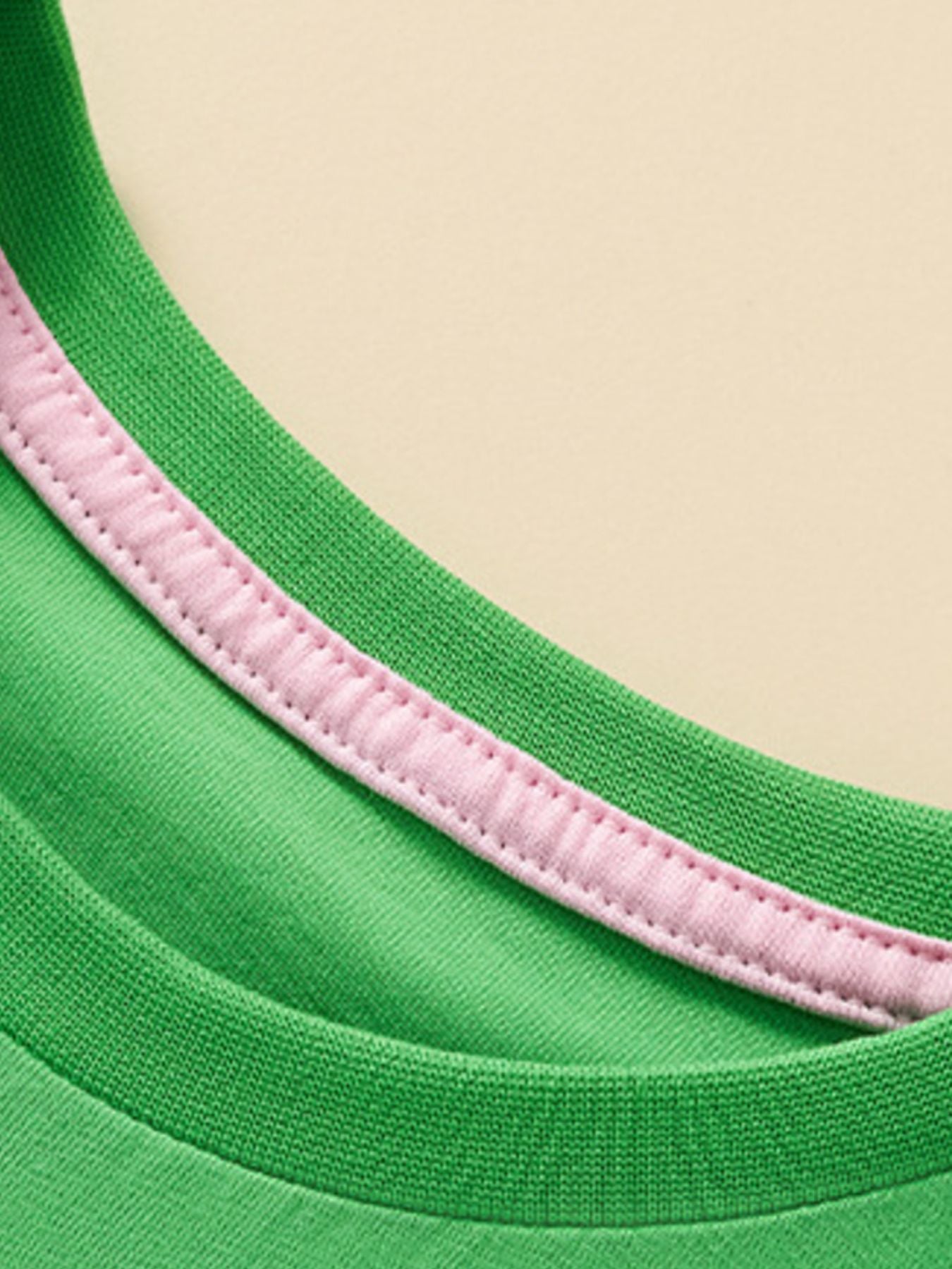 Close view of the green round neckline with pink inner trim and stitching on the children's T-shirt