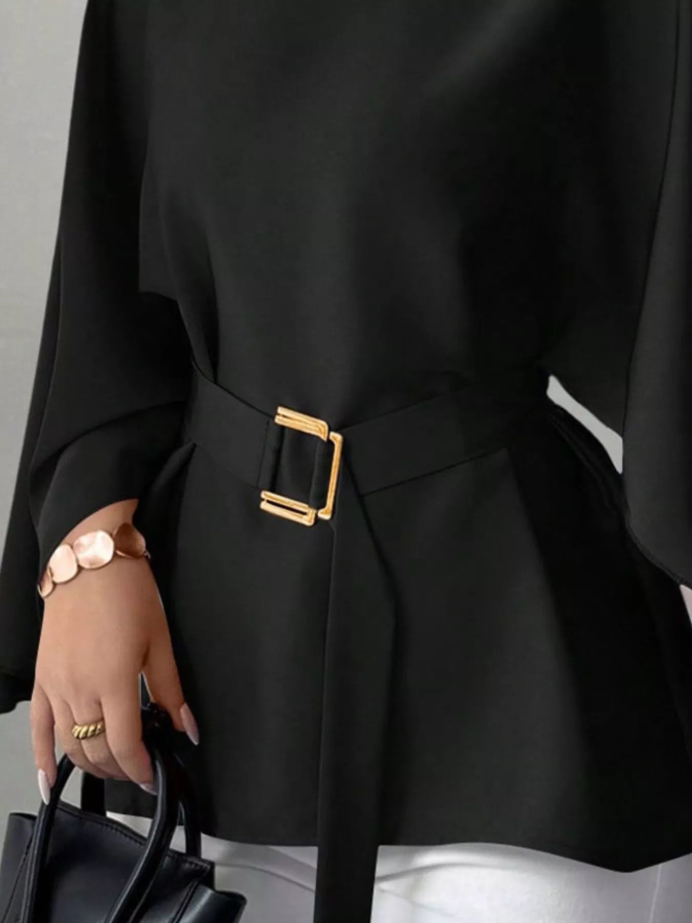 Close detail of black batwing sleeve blouse gold buckle belt and flared peplum hem