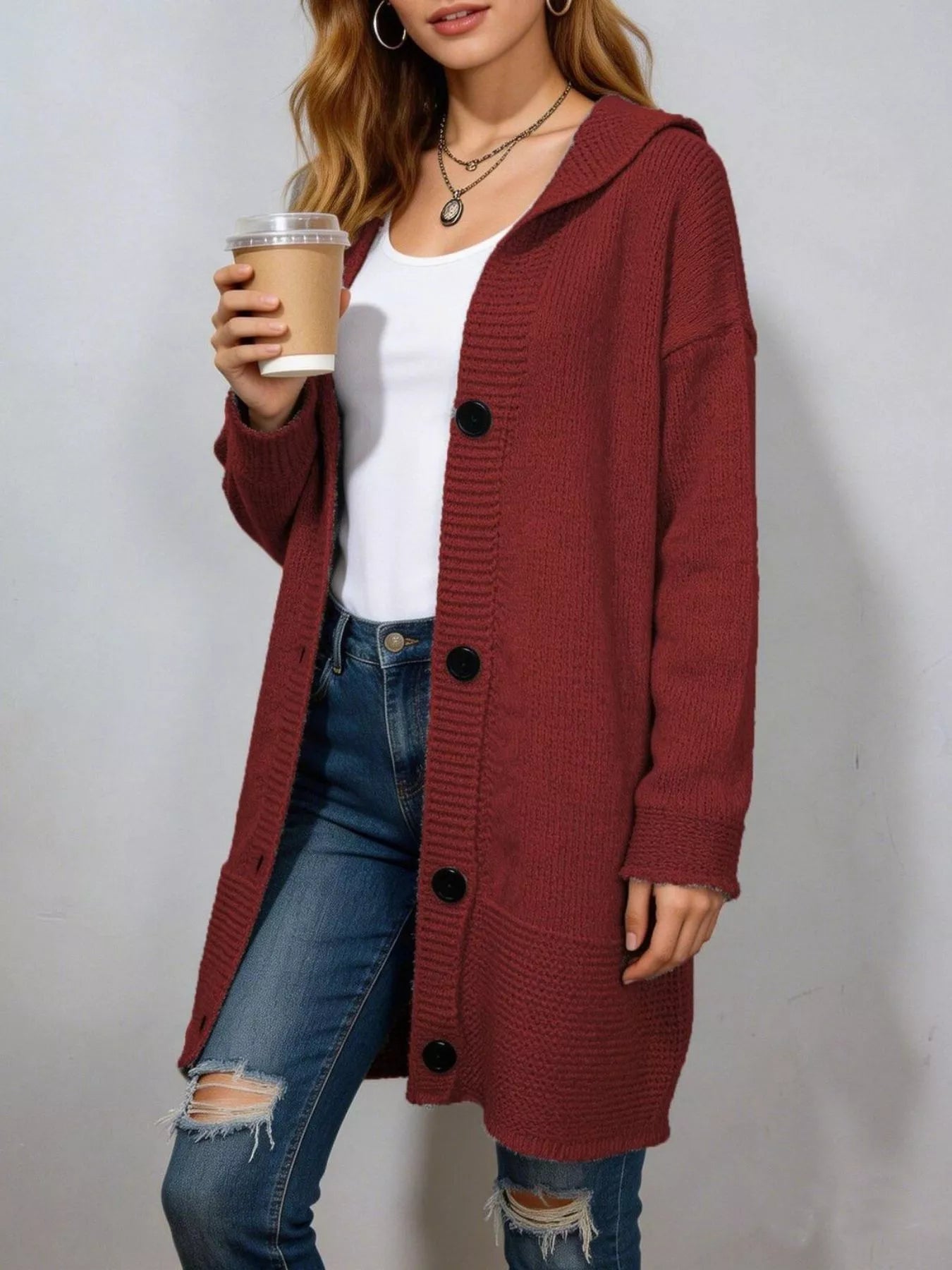 Long burgundy hooded knit cardigan with black buttons worn open over jeans