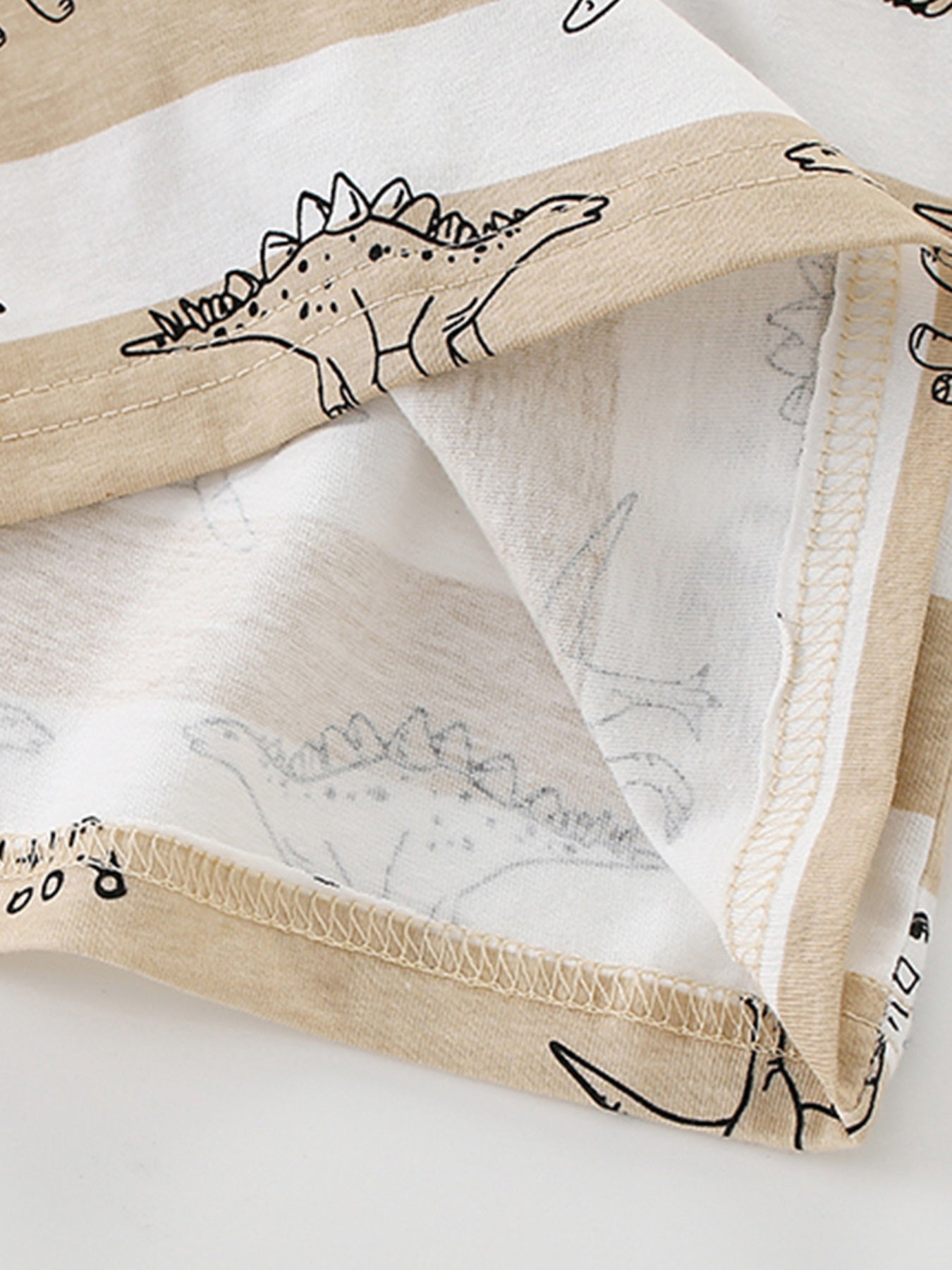 Close-up of the hem stitching and inner fabric on a tan and white striped children's dinosaur T-shirt