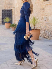 Side view of a dark blue fringed maxi dress with layered fringe worn walking in a courtyard
