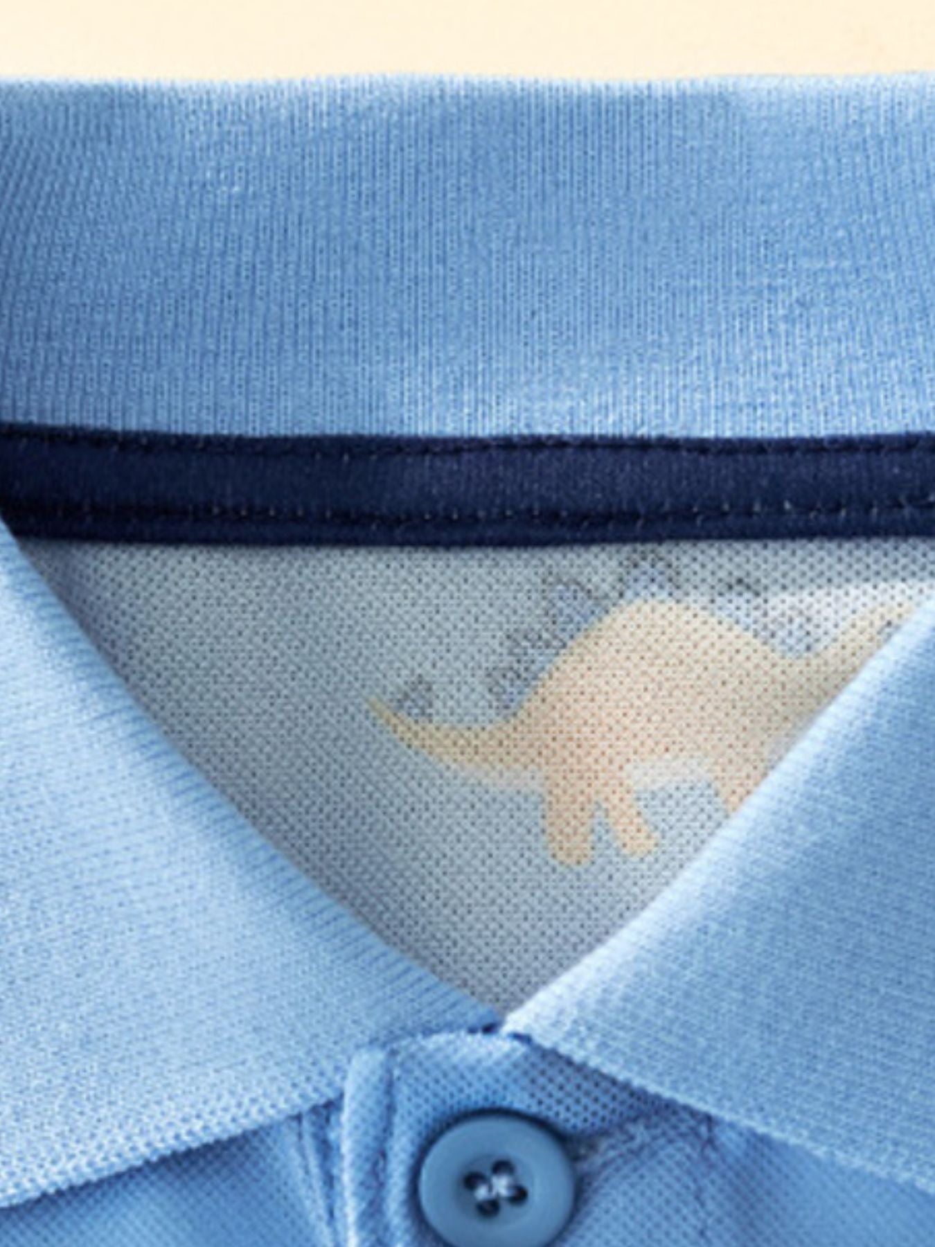 Close-up of the polo collar, inner navy trim, and top button on sky blue fabric