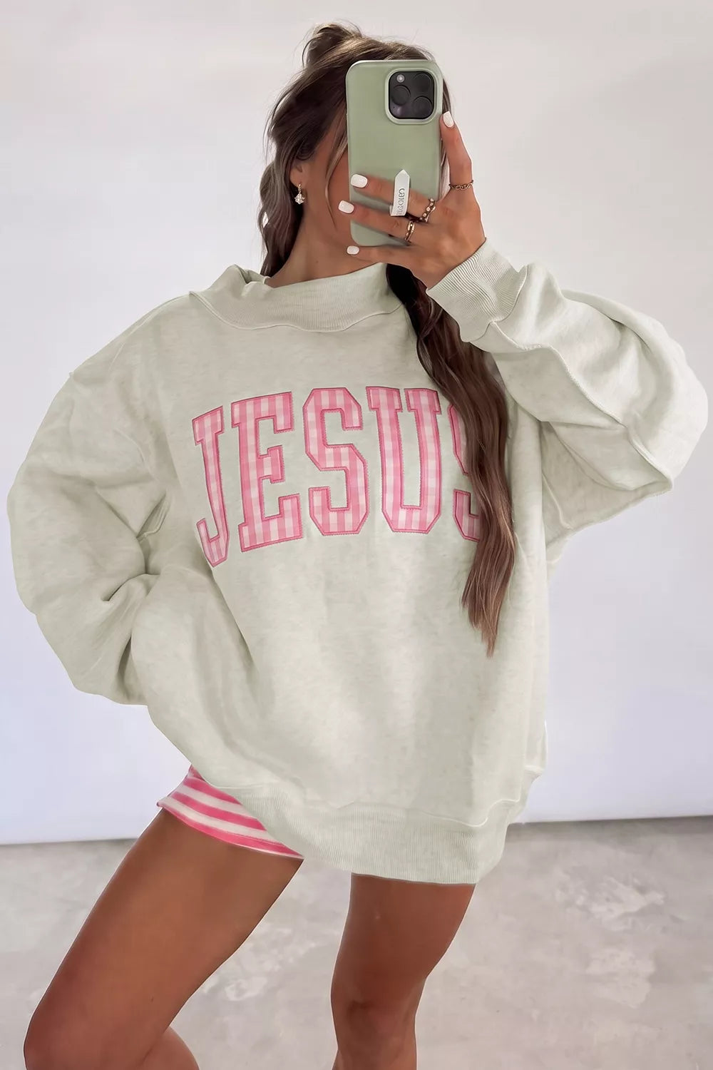 Full front mirror view of beige crew neck sweatshirt with pink gingham JESUS lettering