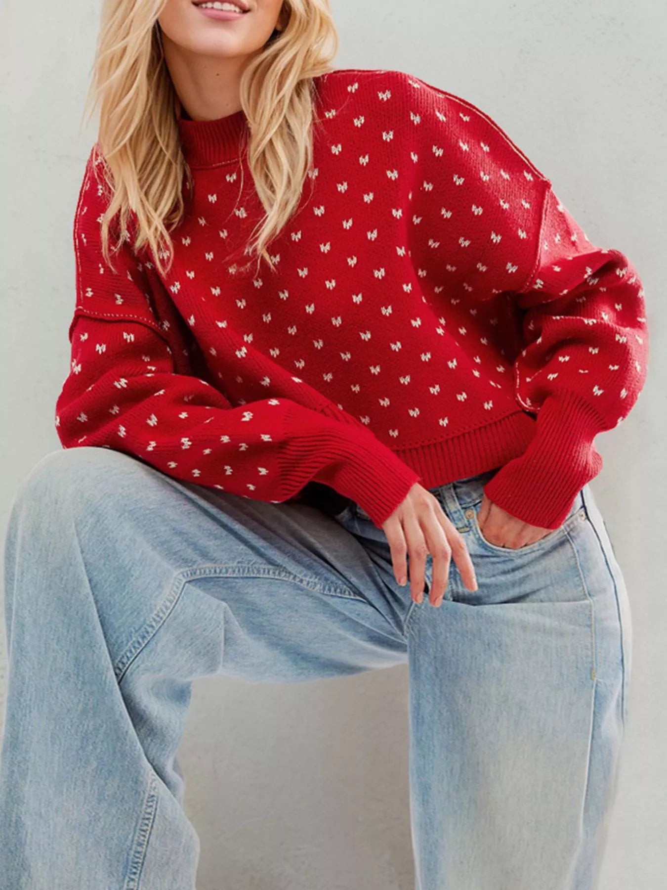 Red dotted knit sweater with ribbed crew neck and cuffs worn seated from the front