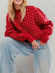 Red dotted knit sweater with ribbed crew neck and cuffs worn seated from the front