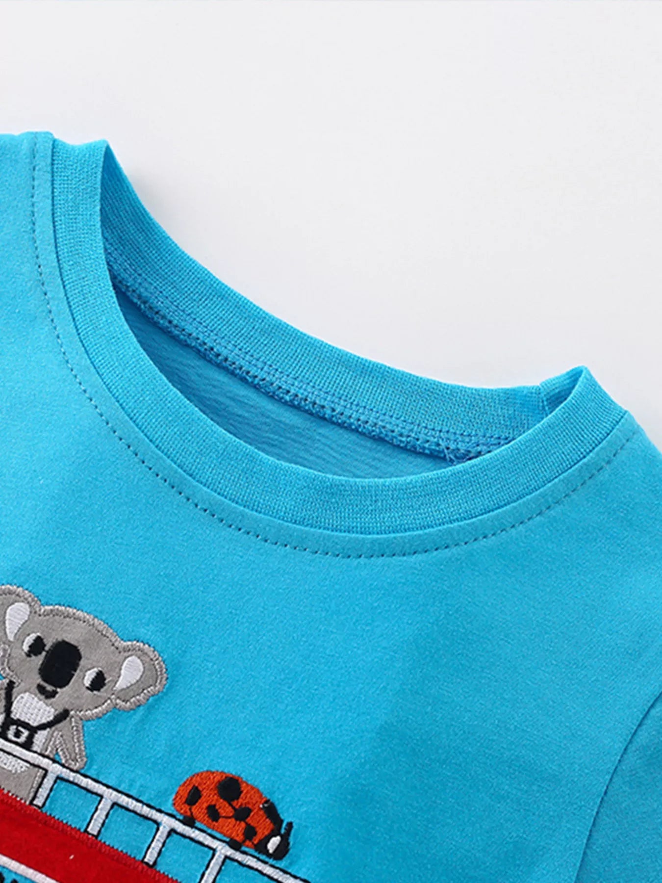 Close-up of ribbed crew neckline and embroidered koala and ladybug on sky blue tee