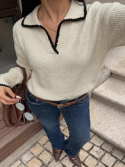 Front view of a cream dropped shoulder sweater with black scalloped trim and ribbed knit