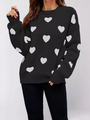 Front view of the black dropped shoulder sweater with white hearts, one arm raised.