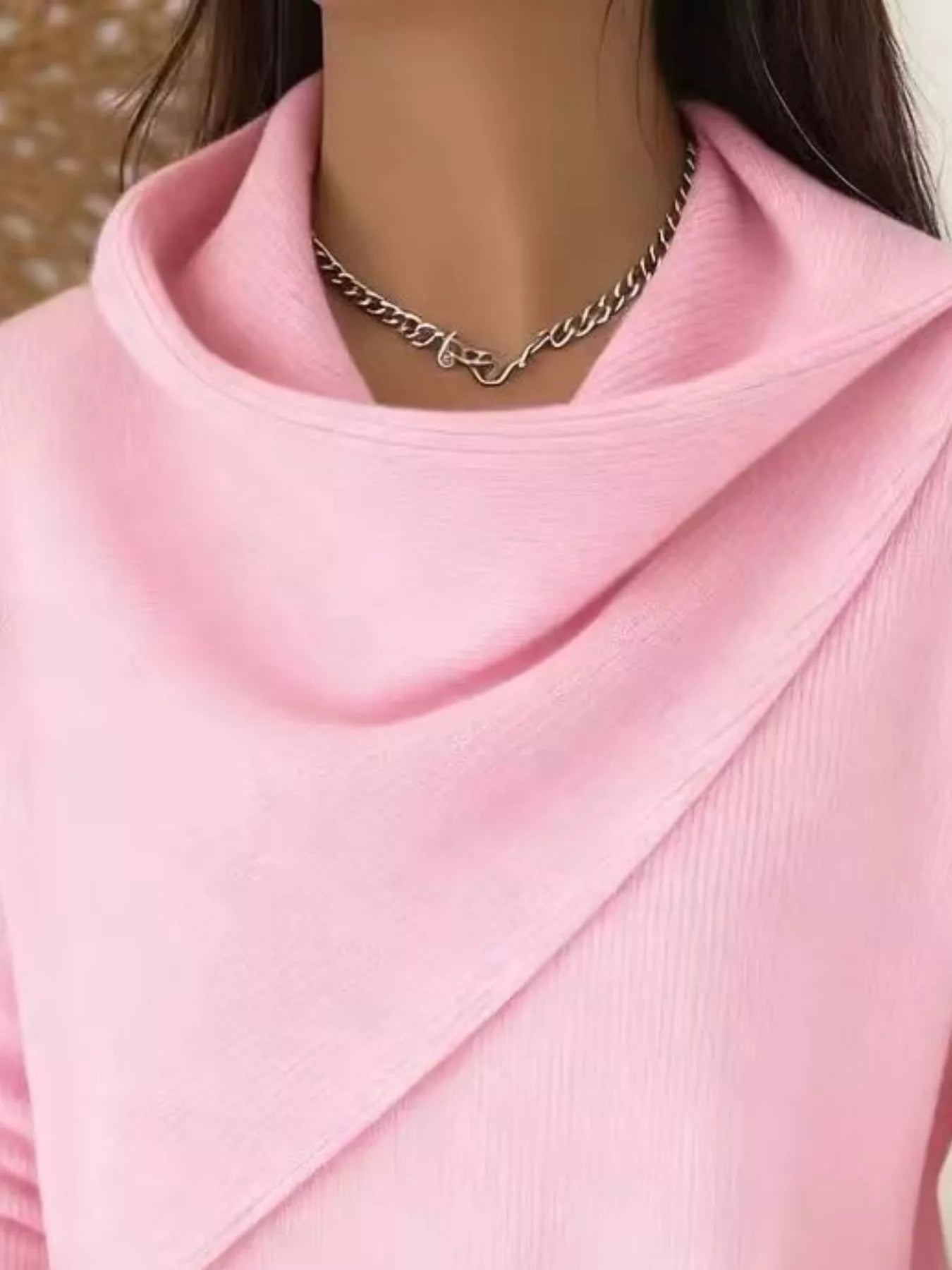 Close-up of the pink cowl neckline showing the draped asymmetric collar and fine knit texture