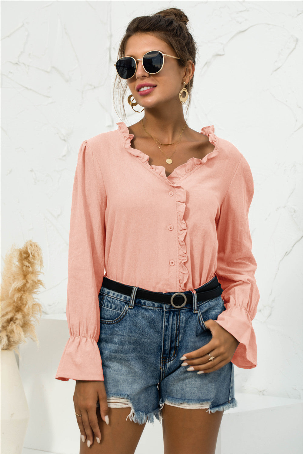 Woman wearing a peach frill-trim V-neck shirt with flounce sleeves, paired with denim shorts.