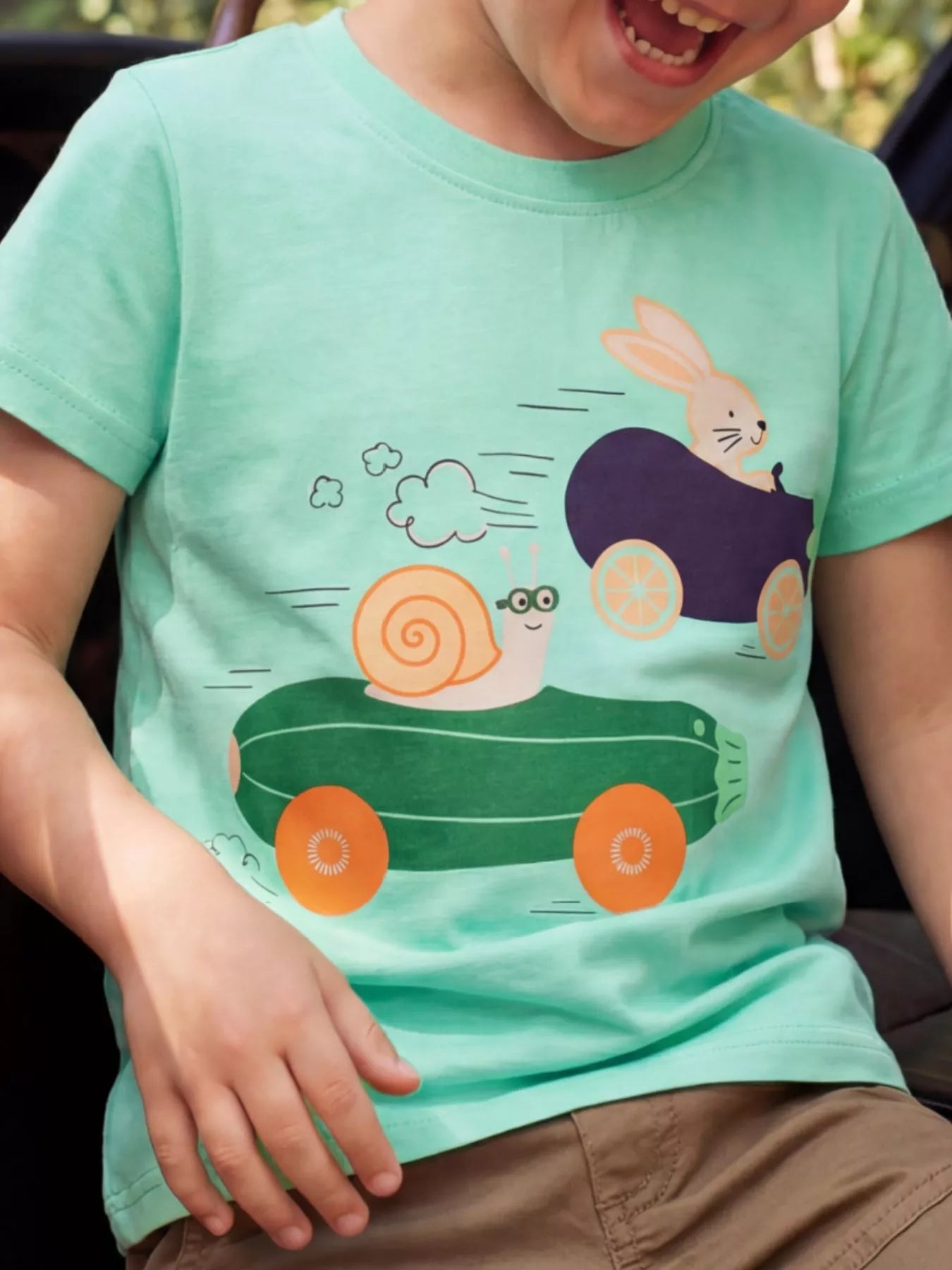 Green children's short sleeve T-shirt shown worn with a snail and bunny racing in vegetable cars
