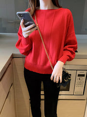 Close front view of the red batwing sleeve knit top with vertical seams, holding a phone indoors.