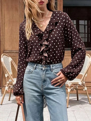 Outdoor front view of a coffee brown polka dot bodysuit with a ruffled V neckline, hand in pocket