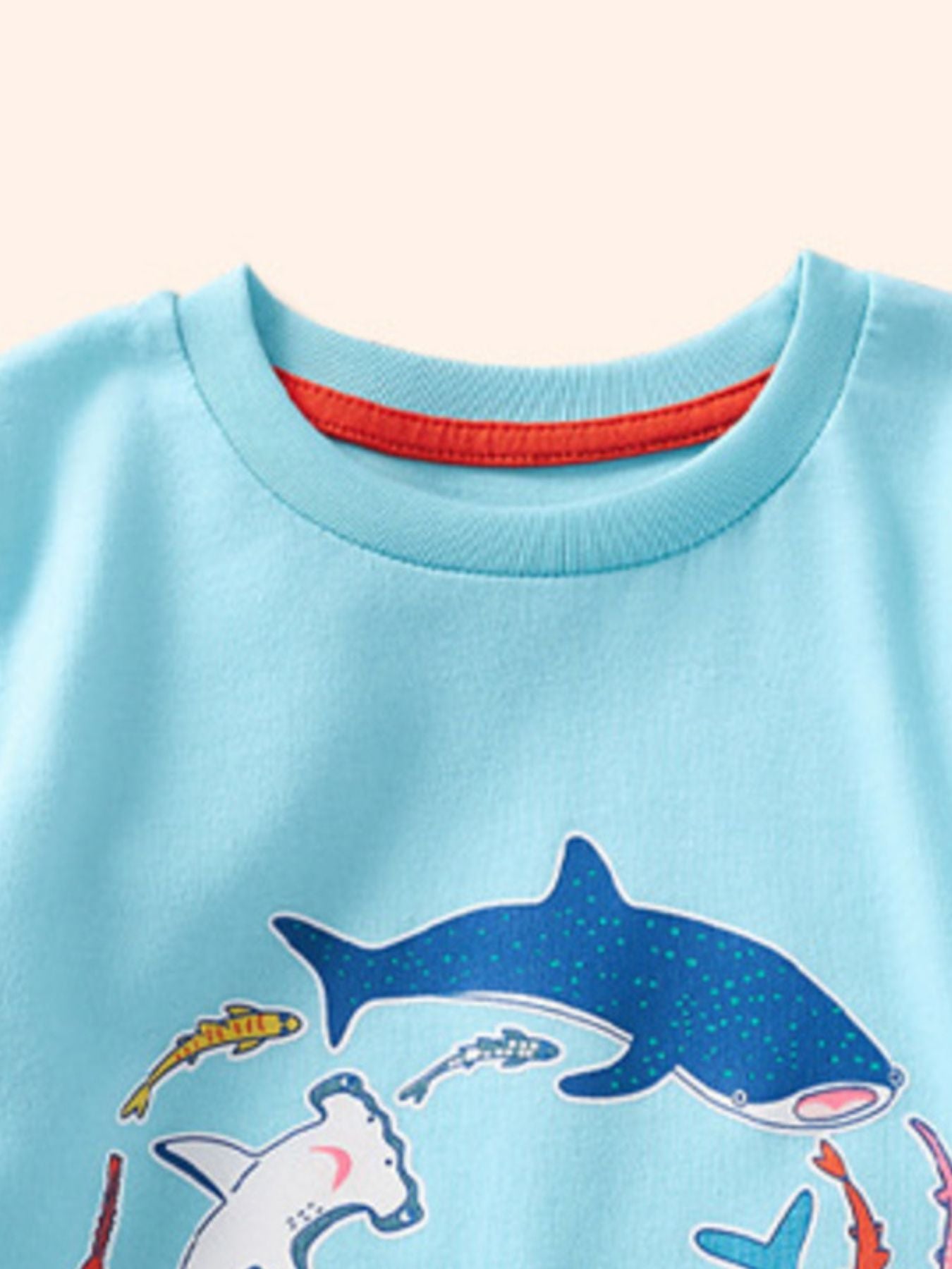 Detail view of the crew neckline with red inner trim on a children's pastel blue shark print t-shirt