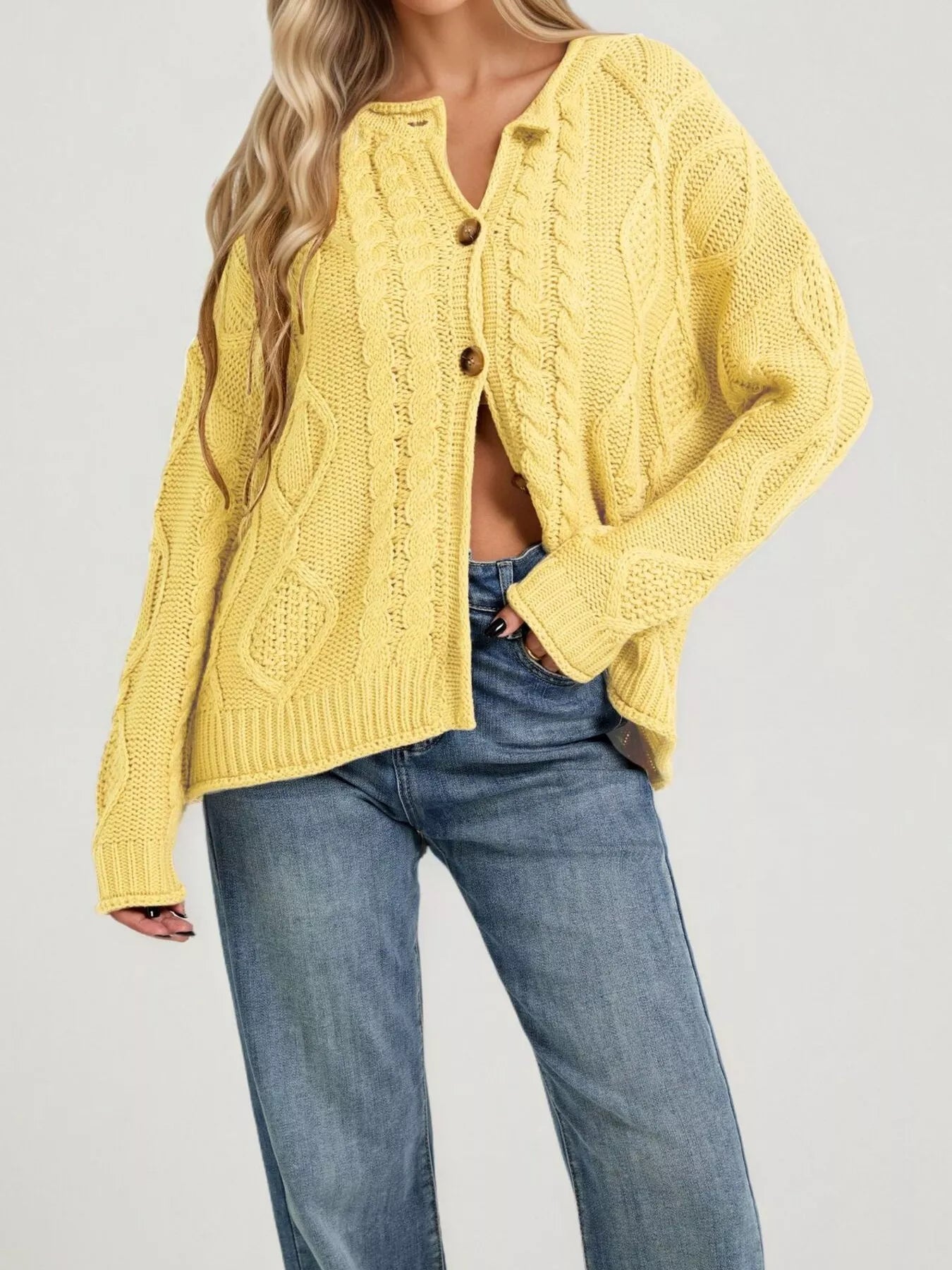 Front view of yellow cable knit button down cardigan with brown buttons and blue jeans
