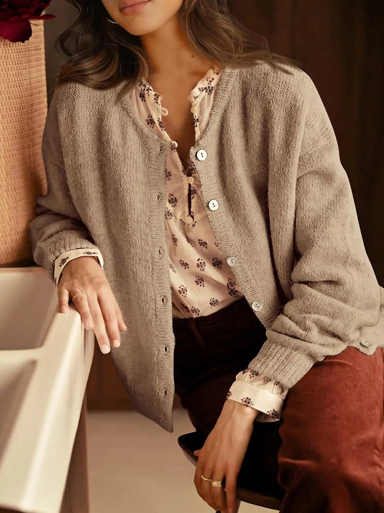 Open khaki button down cardigan worn over a floral blouse while seated indoors