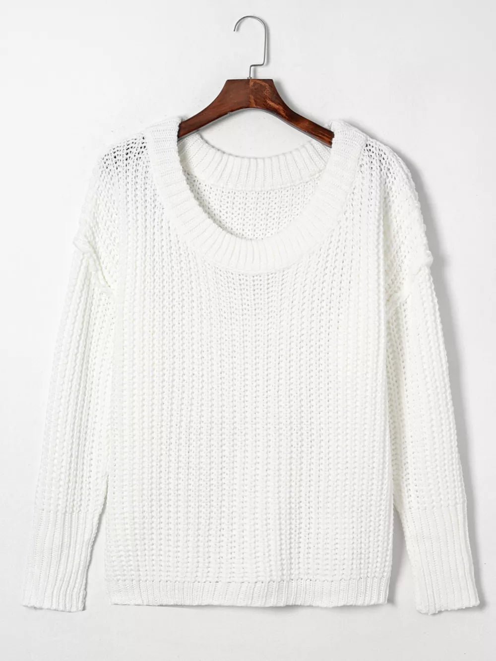 White ribbed knit sweater with round neckline and long sleeves hanging on a wooden hanger.