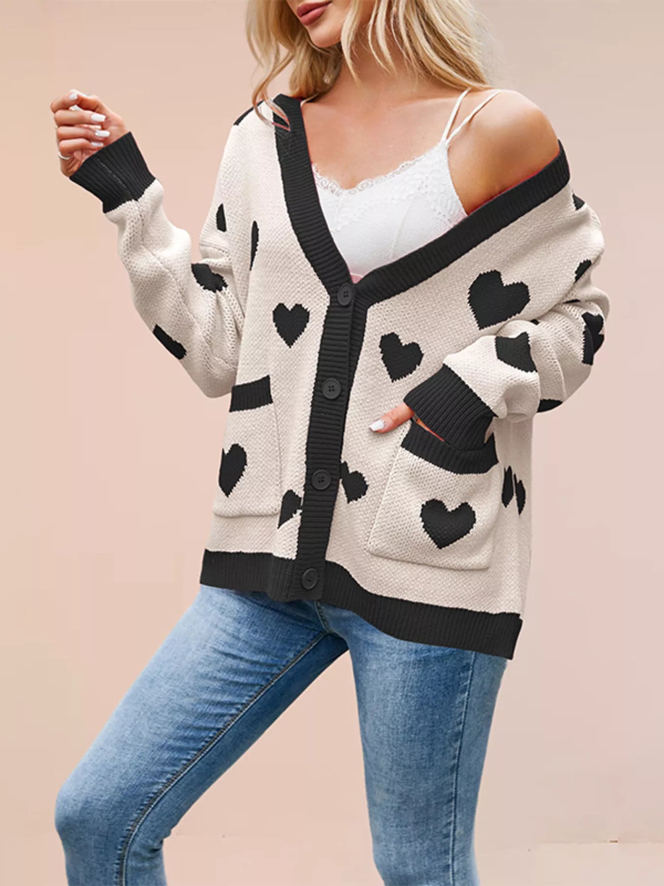 Cream knit cardigan with black hearts buttoned with hand in pocket