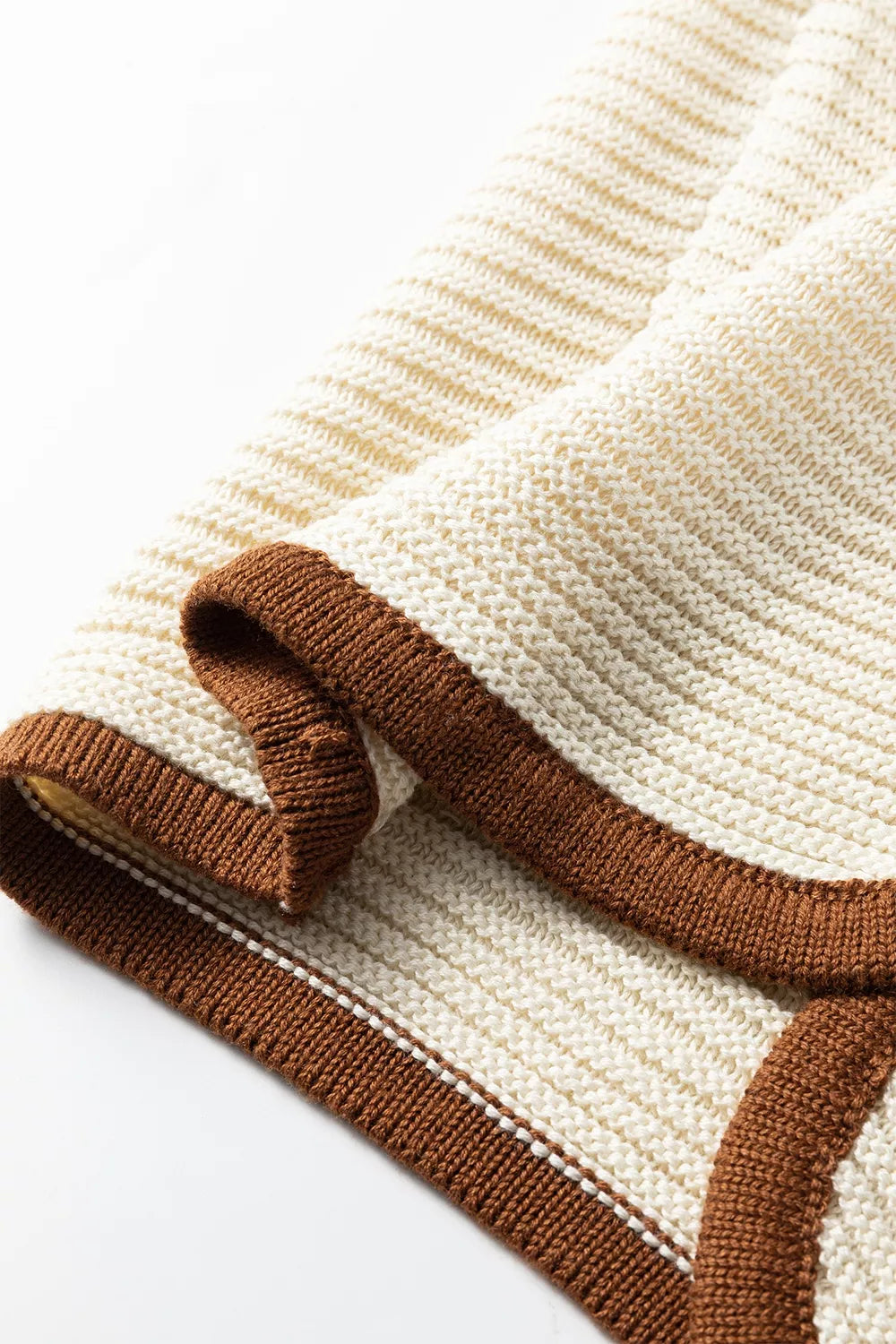Close up detail of a beige sweater vest hem with brown contrast trim and knit texture