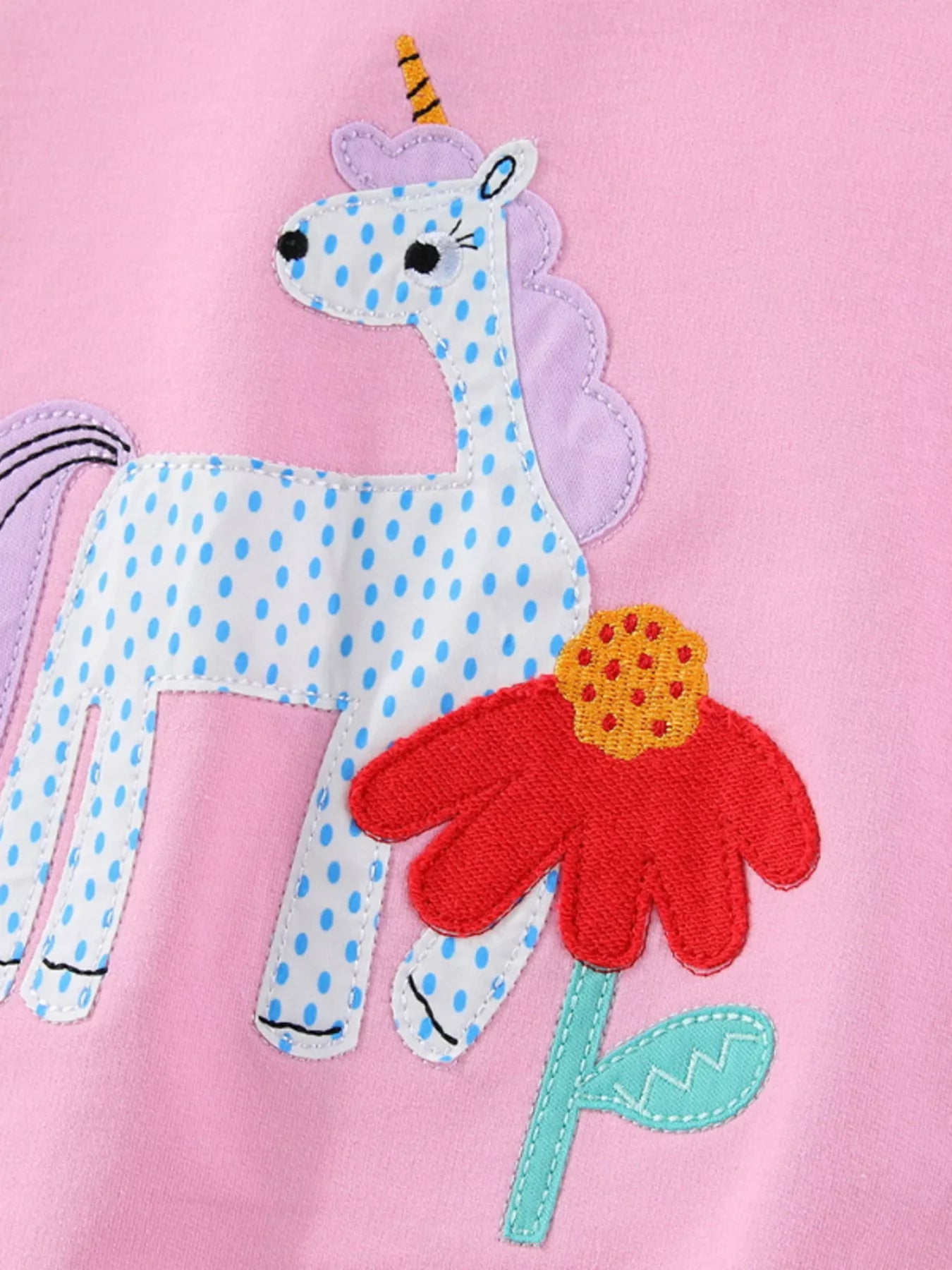 Close view of the spotted unicorn and red flower patch on pink fabric