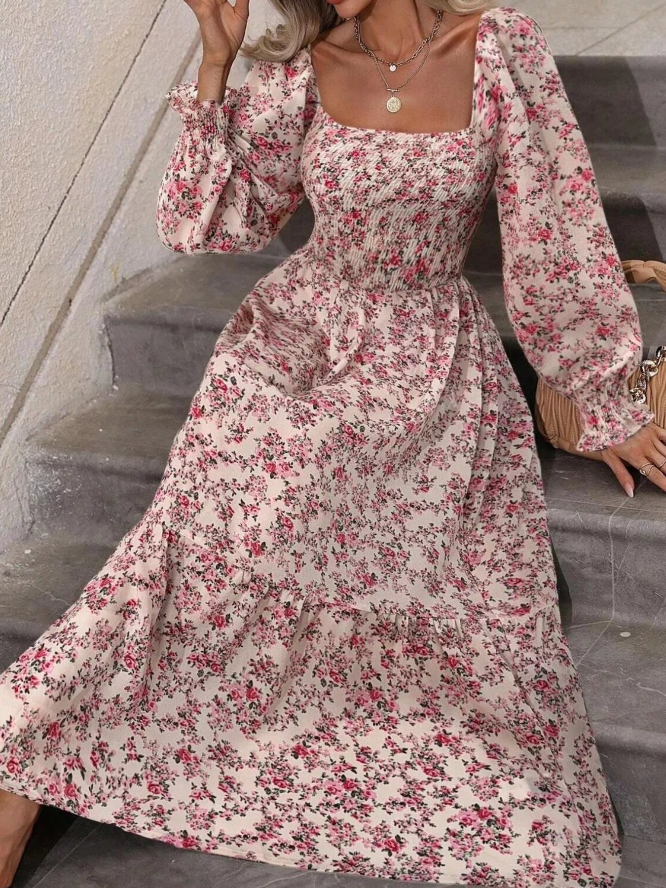 Pink floral midi dress with smocked bodice, model seated on stone steps