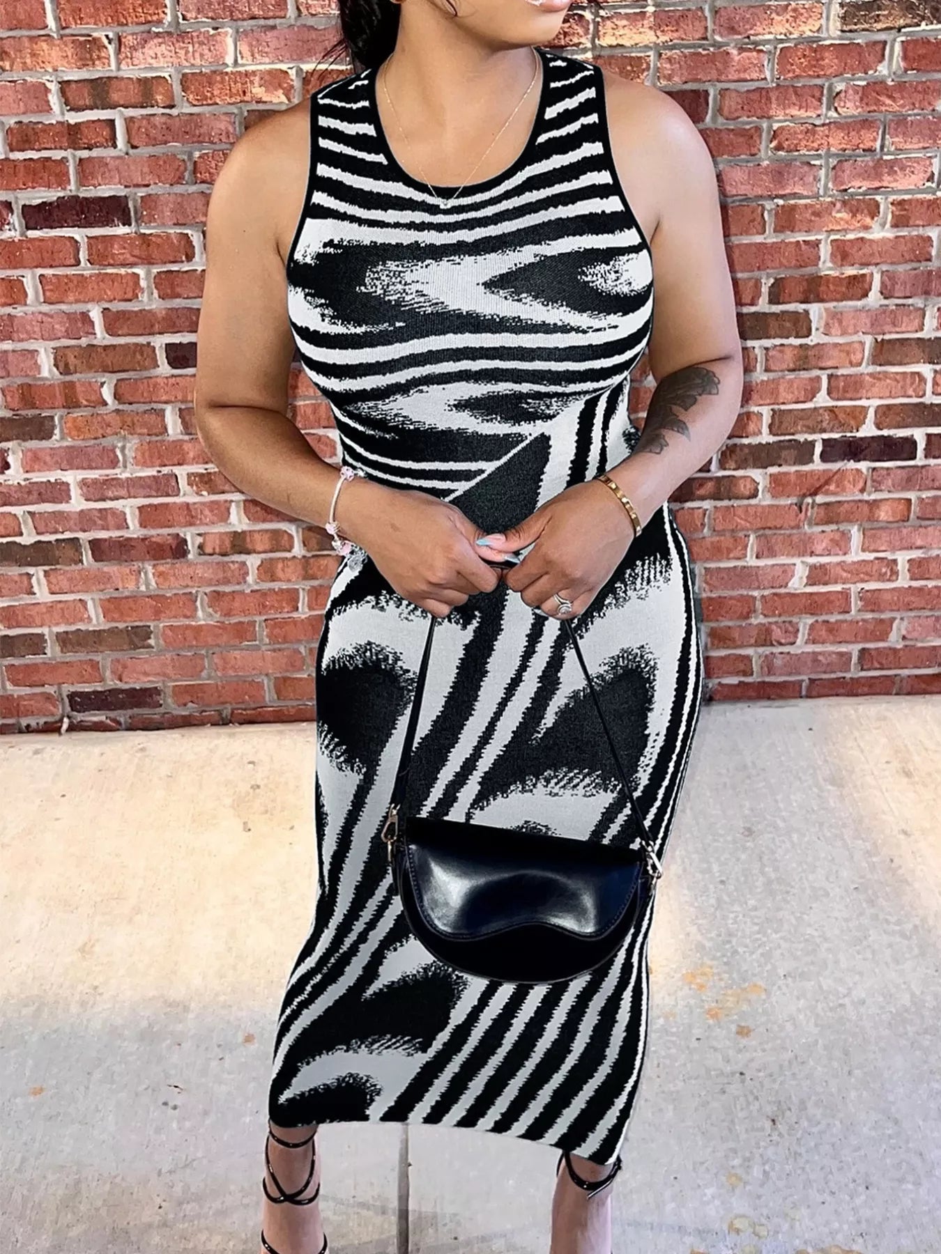 Front view of a plus size black and white sleeveless bodycon maxi dress with a black crossbody bag