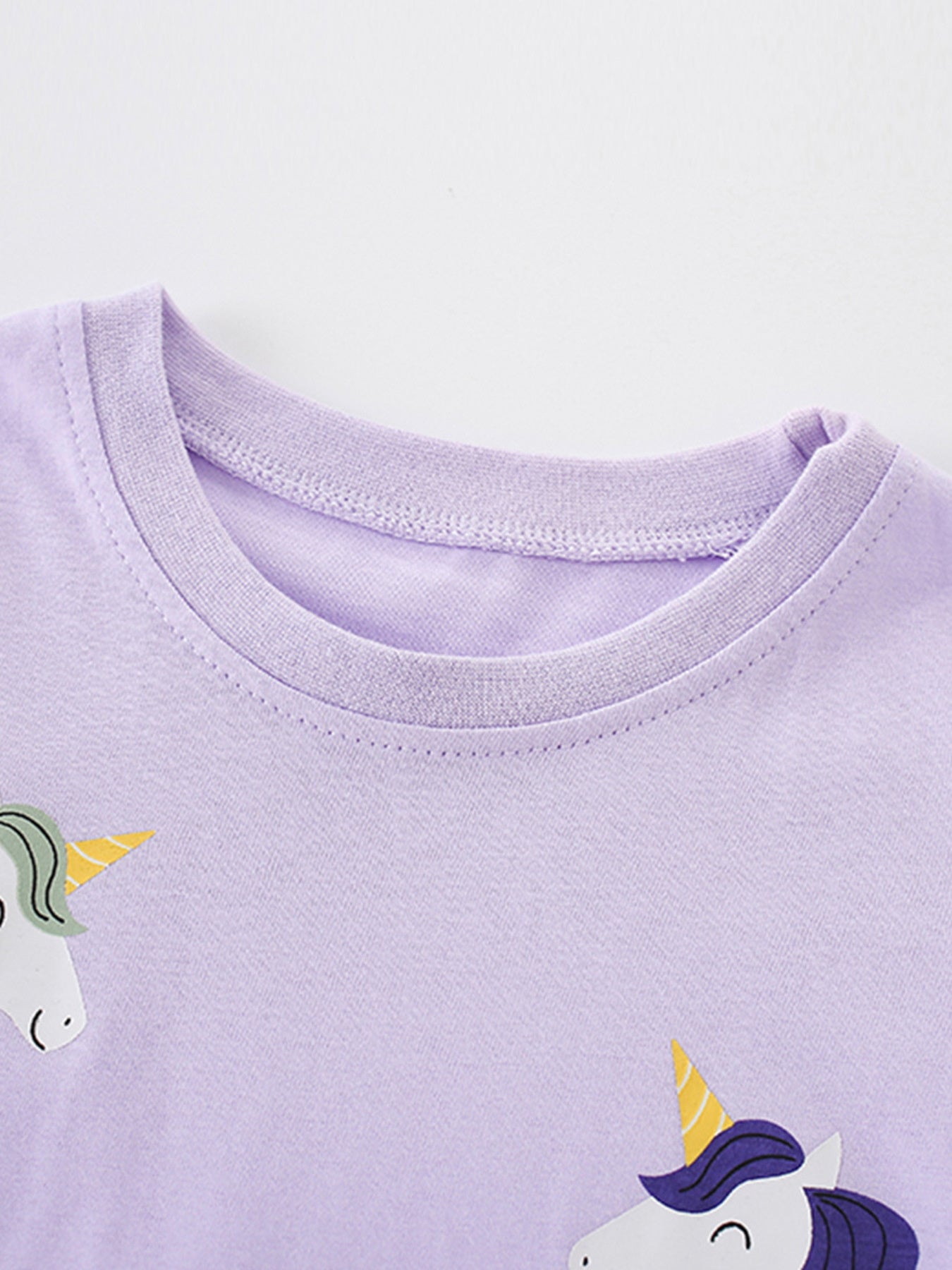 Close view of the round neckline with unicorn heads at the edges of the light purple T-shirt